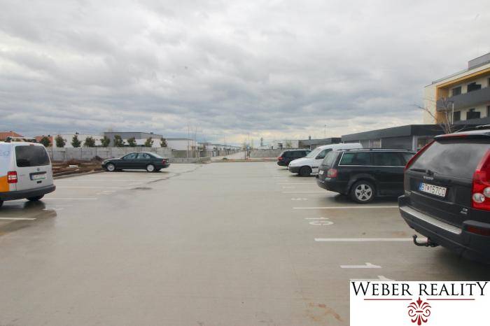 Parkoló a Broskyňová utcában, Rovinka városában, autókkal és lakóépületekkel a háttérben.