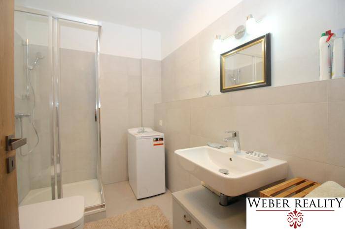 Fürdőszoba mosdóval, mosógéppel és zuhanyzóval egy egyszobás lakásban.