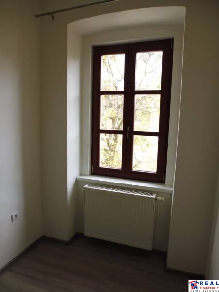Szoba nagy ablakkal, radiátorral és fa dekorációjú padlóval egy háromszobás lakásban.