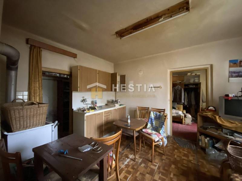 Konyha egy családi házban, fa bútorokkal, régi televízióval, étkezőasztallal és szekrénnyel.