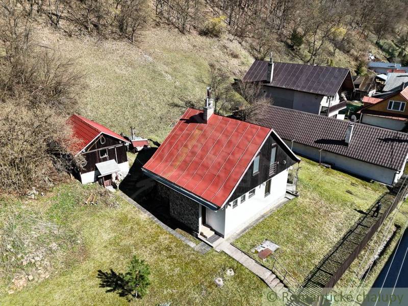 Ház Moštenicában ferde piros tetővel, környező zöld növényzet és lejtős terep.