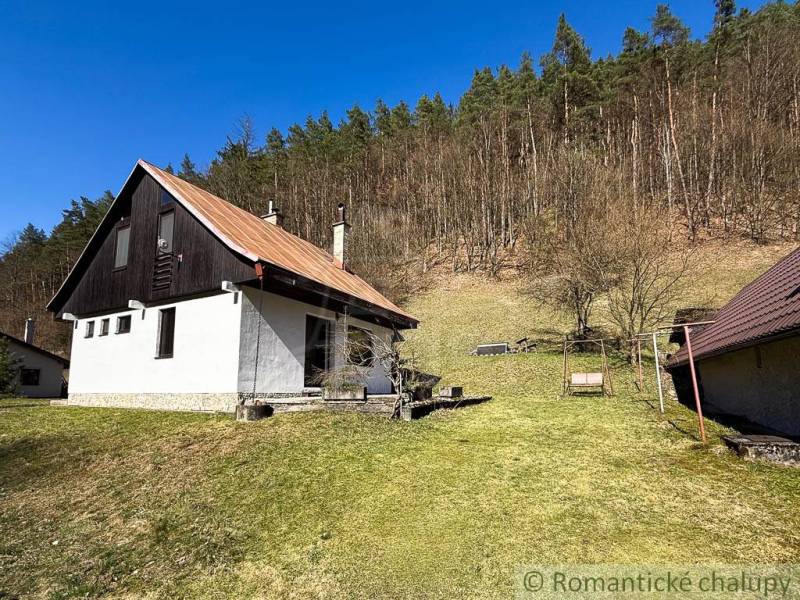 Házikó Moštenicában, füves területtel körülvéve, háttérben erdővel.