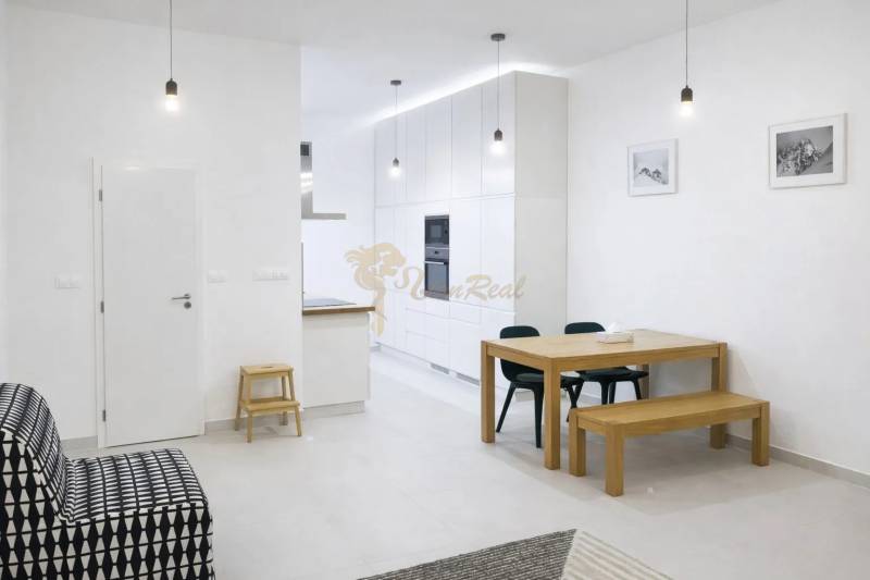 Egy 2 szobás lakás belső tere fehér falakkal, fa asztallal és fekete kanapéval.