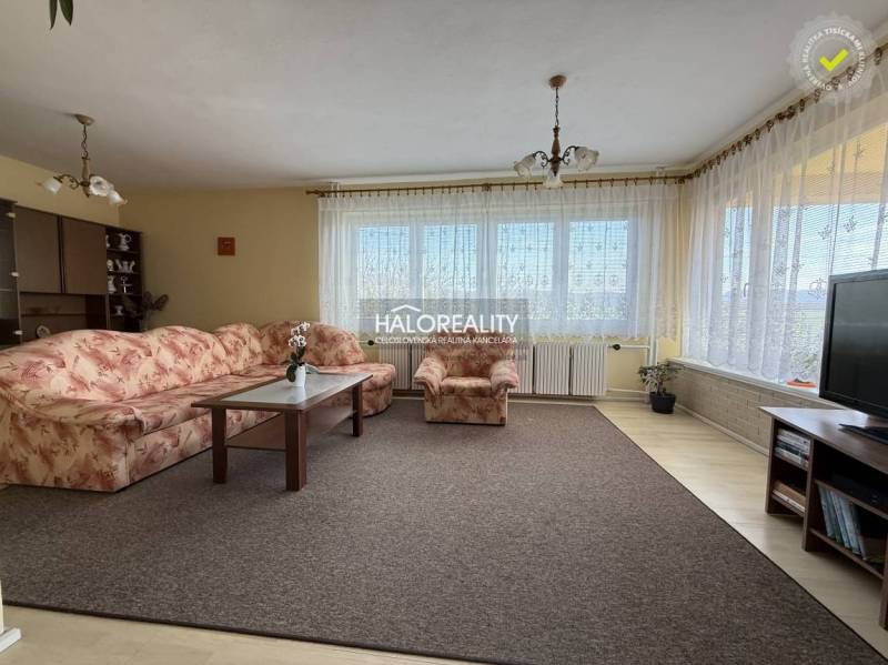 Nappali szőnyeggel, virágmintás kanapéval és fa dekoros padlóval egy családi házban.