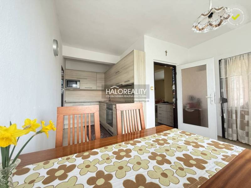 Világos konyha családi házban, fa bútorokkal és dekoratív asztalterítővel.