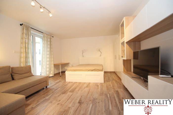 Nappali zóna egyszobás lakásban ággyal és fa dekor padlóval.