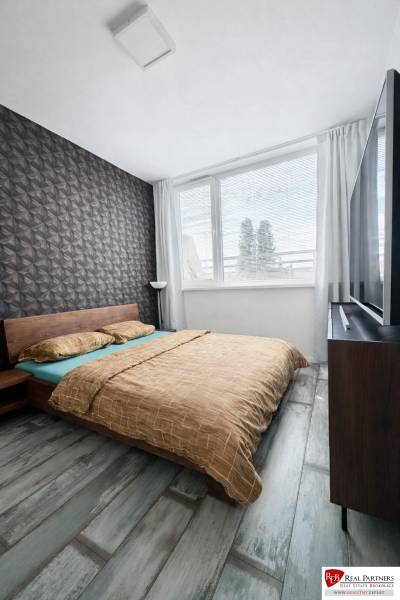 Hálószoba egy kétszobás lakásban geometrikus tapétával és fa dekorációjú padlóval.