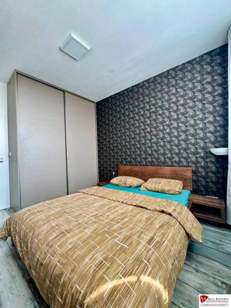 Hálószoba egy kétszobás lakásban ággyal és mintás tapétával, fa dekorációjú padlóval.