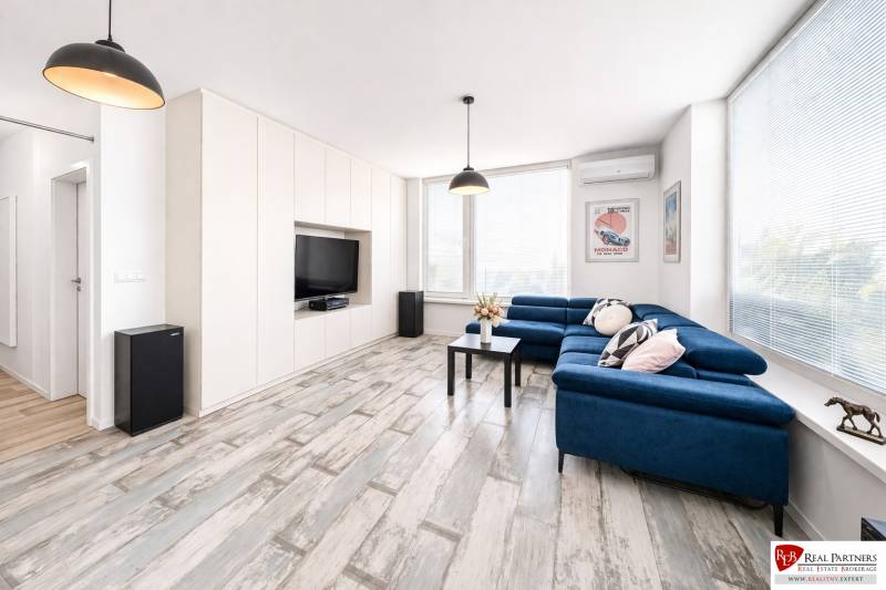 Nappali egy kétszobás lakásban kék kanapéval és fa dekorációjú padlóval.