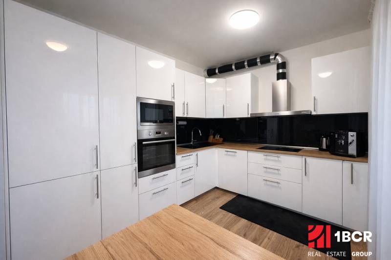 Konyha egy háromszobás lakásban fehér szekrényekkel és fa mintázatú padlóval.