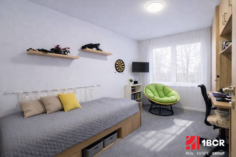 Gyerekszoba egy háromszobás lakásban ággyal, játékokkal és zöld fotellel.