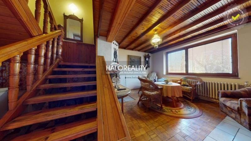 Családi ház belső tere lépcsővel, fa dekorációjú padlóval és rattan bútorokkal.