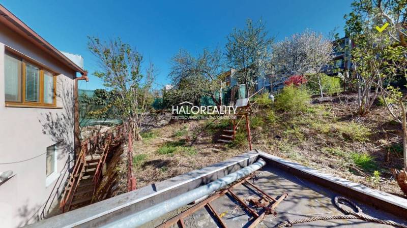 Családi ház Rimaszombatban, egy lejtős kert mellett, fákkal.