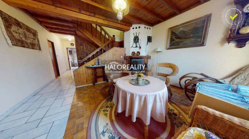 Családi ház fa mintázatú padlóval, rattan bútorokkal, kandallóval, szőnyeggel, fa mennyezettel.