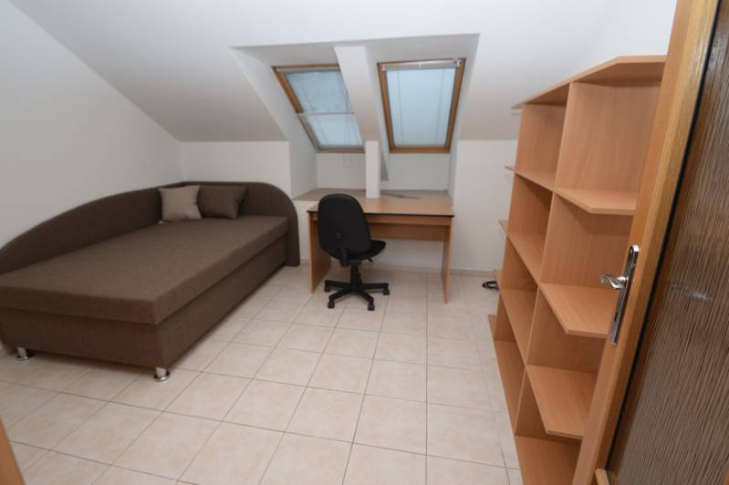 Szoba családi házban ággyal, asztallal, polcokkal, csempével és tetőablakokkal.