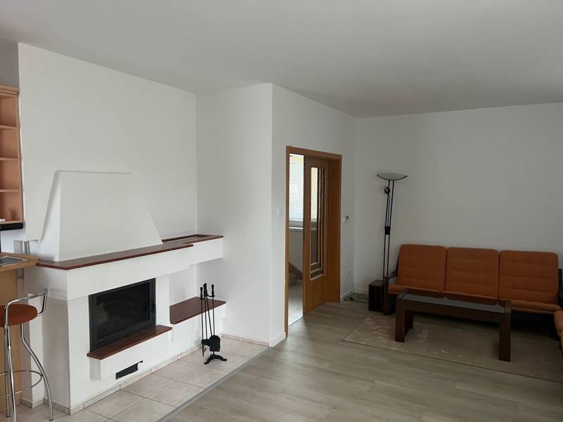 Nappali kandallóval, narancssárga kanapéval, fa mintás padlóval és üvegasztallal.