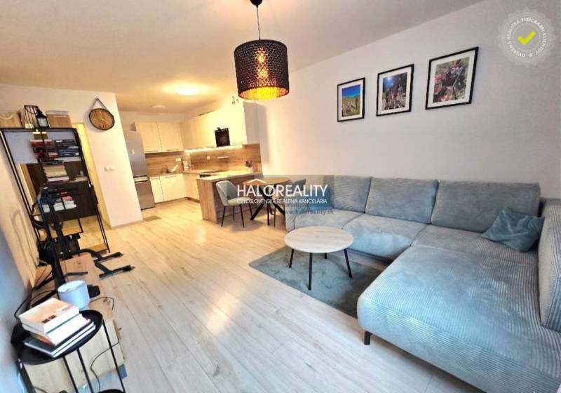 Nappali sarokkanapéval, konyhával és fa dekoros padlóval egy kétszobás lakásban.