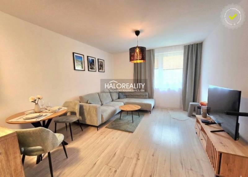 Nappali egy kétszobás lakásban sarokkanapéval és televízióval, fa mintázatú padlóval.