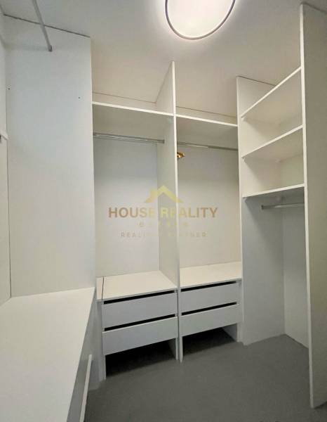 Beépített fehér polcokkal és fiókokkal rendelkező gardrób egy háromszobás lakásban.