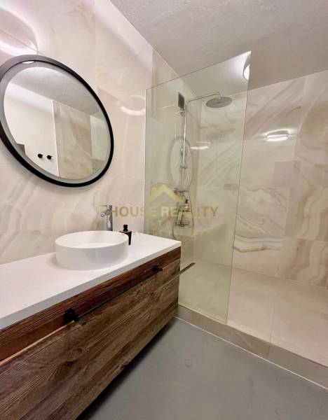 Fürdőszoba fa szekrénnyel, kör alakú tükörrel és zuhanyzóval egy háromszobás lakásban.