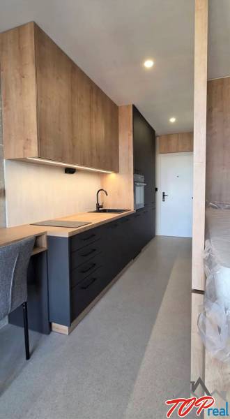 A garzonlakásnak van egy konyhapultja fa mintázatú padlóval és beépített háztartási gépekkel.