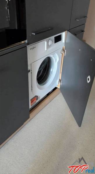 Beépített mosógép szürke ajtók mögött egy garzonlakásban egyszerű padlóval.