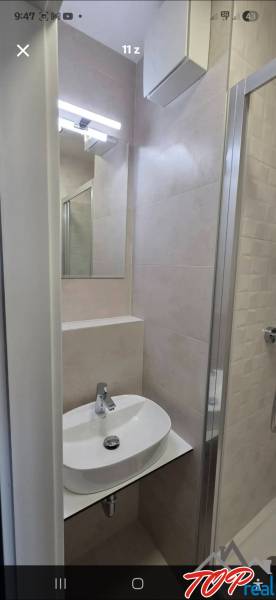 Kompakt fürdőszoba garzonlakásban mosdóval, tükörrel és zuhanyzóval.