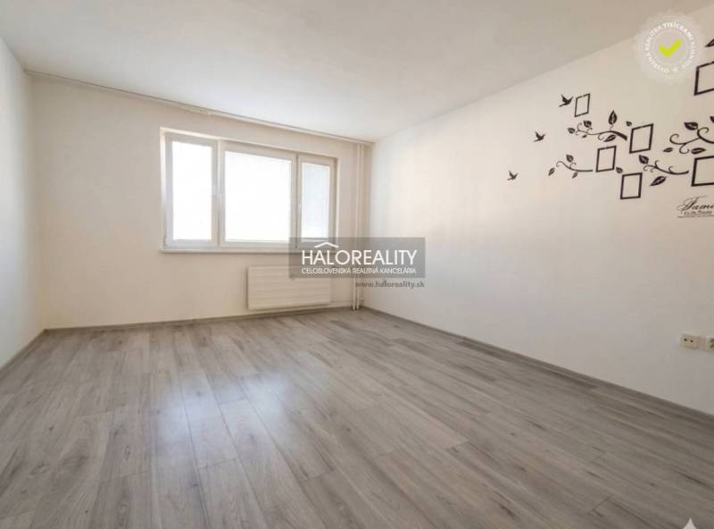 Szoba egy háromszobás lakásban fa dekoros padlóval és fehér falakkal.