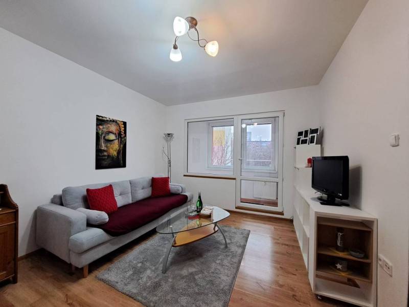 Nappali egy kétszobás lakásban kanapéval, üvegasztallal és fa dekorációjú padlóval.