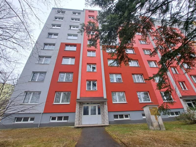 Egy piros homlokzatú lakóház Poprádon, amely előtt járda és fák vannak.