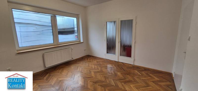 Szoba egy háromszobás lakásban fehér falakkal és fa dekorációjú padlóval.