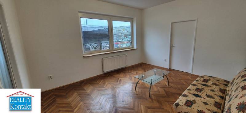Nappali kanapéval, üvegasztallal és fa dekorációjú padlóval egy háromszobás lakásban.