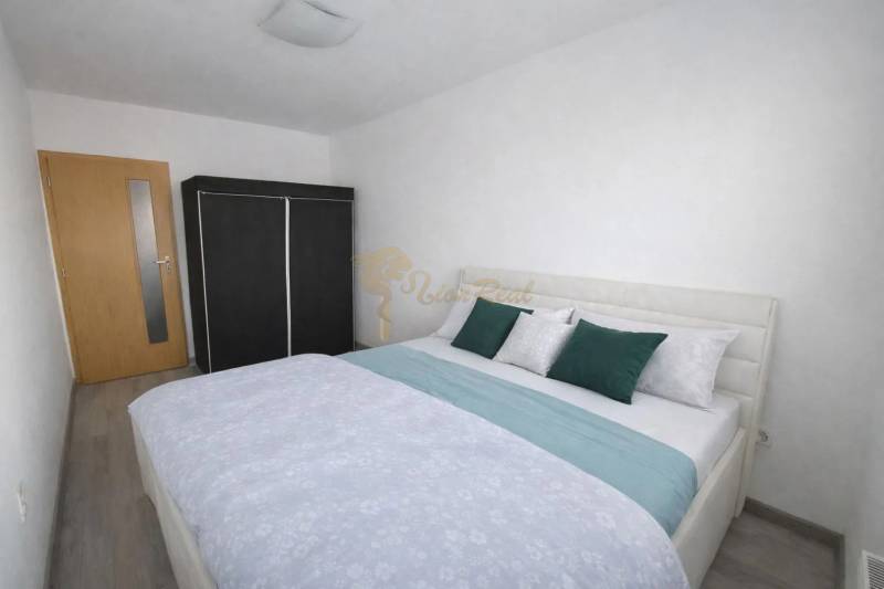 Hálószoba ággyal, beépített szekrénnyel és fa dekorációjú padlóval egy háromszobás lakásban.