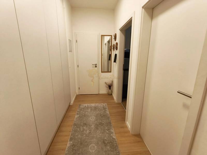 Két szobás lakás folyosója fa mintás padlóval és nagy tükörrel.