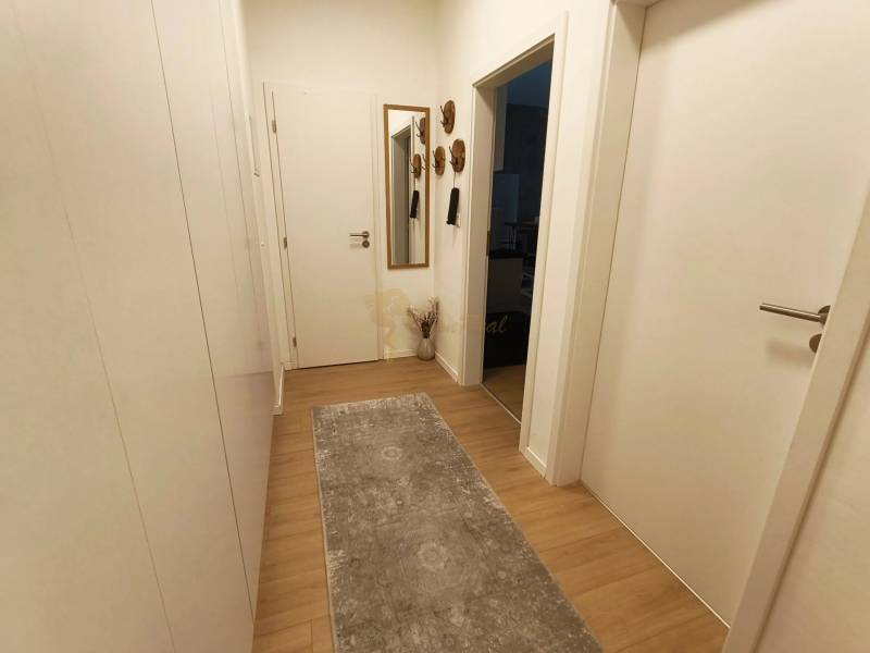 Két szobás lakás folyosója fa dekor padlóval, tükörrel és fehér ajtókkal.