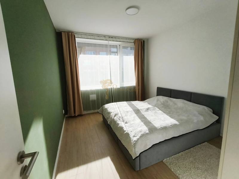 Hálószoba egy kétszobás lakásban, ággyal és ablakkal, fa hatású padlóval.