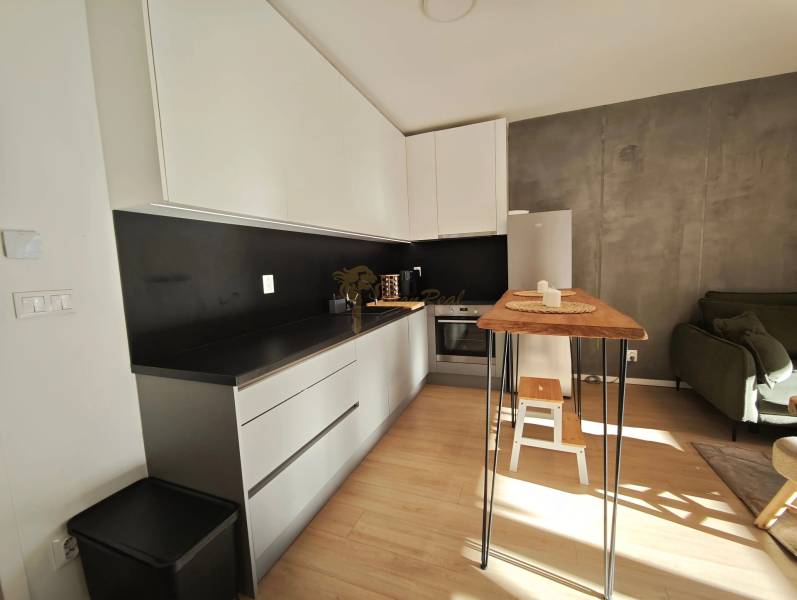 Konyha egy kétszobás lakásban fekete részletekkel és fa dekorációjú padlóval.