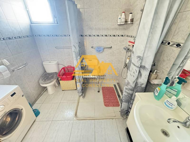 Családi ház fürdőszobája mosógéppel, zuhanyzóval és WC-vel.