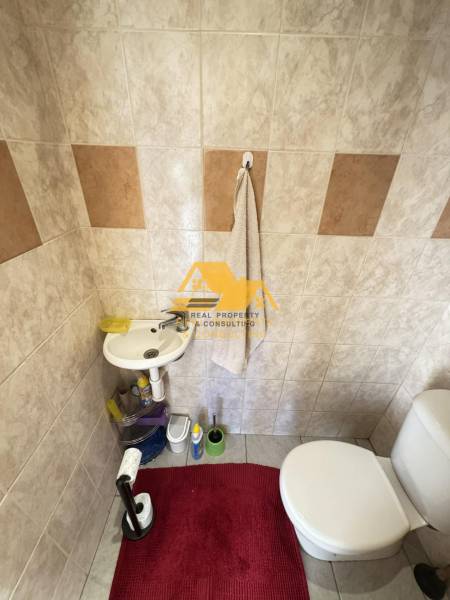 Fürdőszoba mosdóval és WC-vel, a csempék világos és barna árnyalatokat kombinálnak.