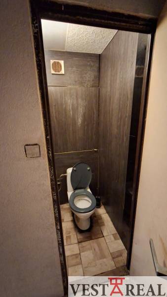 Kerámia burkolatú WC egy háromszobás lakásban, sötét burkolat és szellőzés.