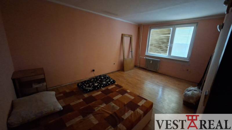 Szoba fa dekorációjú padlóval, egyszerű ággyal és komóddal egy háromszobás lakásban.