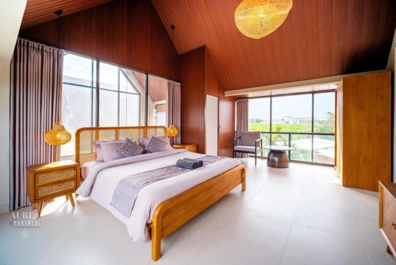 Hálószoba egy villában nagy ablakokkal, fa elemekkel és ágyneművel ellátott ággyal.