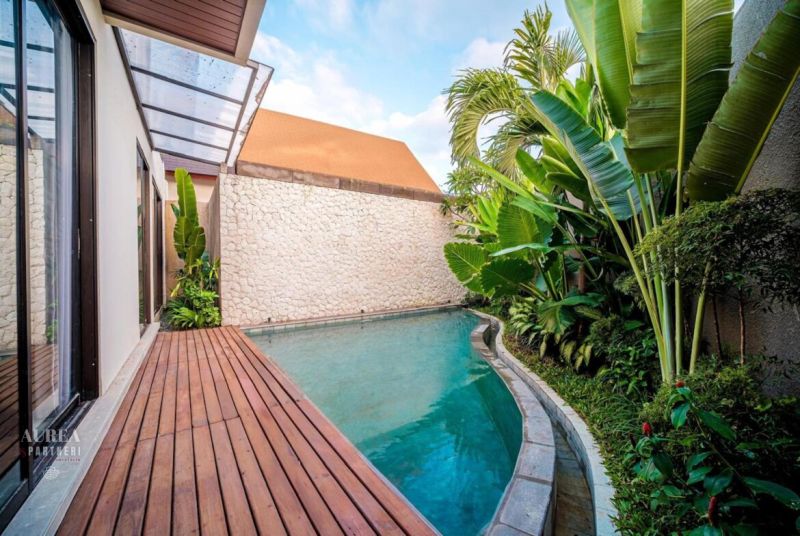 Bali villa medencével, zölddel körülvéve és fa dekorációjú padlóval.