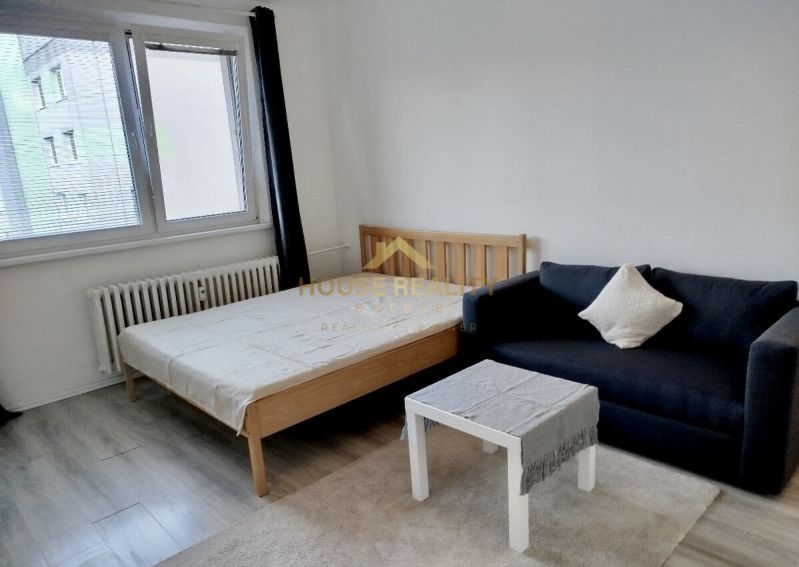 Szoba ággyal, fekete kanapéval és asztallal, fa dekorációjú padlóval.