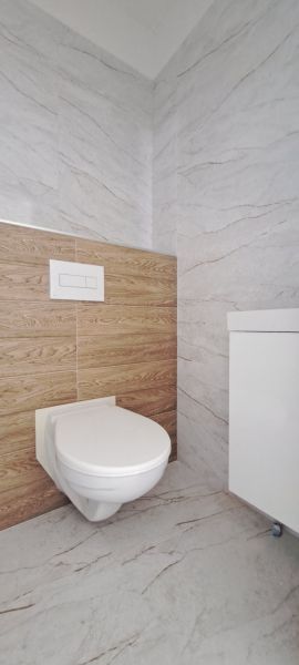 Családi ház fürdőszobájában található WC márvány- és fa burkolatokkal.