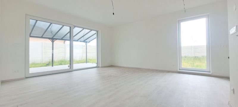 Tágas szoba nagy ablakokkal és fa dekorációjú padlóval egy családi házban.