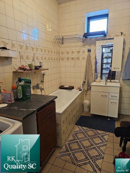 Családi ház fürdőszobája káddal, mosdóval és tárolószekrényekkel. Csempézett falak.