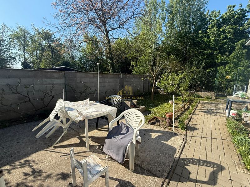 A szekuliai nyaraló kertje műanyag bútorokkal és a szélén fákkal.