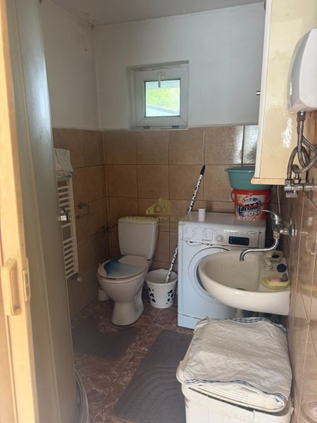 Fürdőszoba a házban WC-vel, mosógéppel és mosdóval. Csempe a falakon.