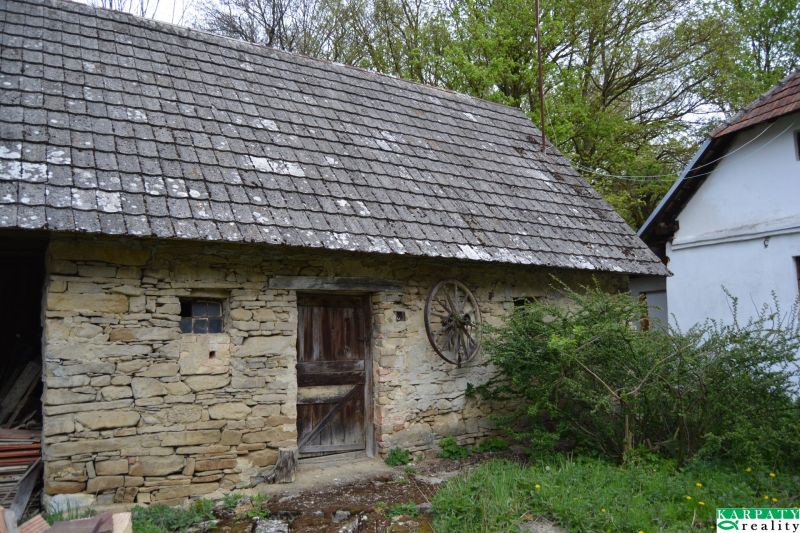 Kőből épült pajta egy családi ház mellett Bukovecben, faajtókkal és cseréptetővel.